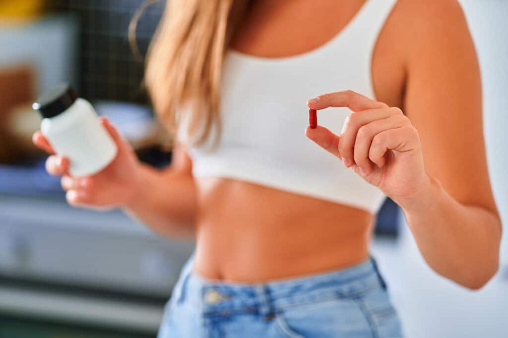 Nő tart egy piros tablettát és egy fehér üveget Clenbuterol fogyás kapcsán